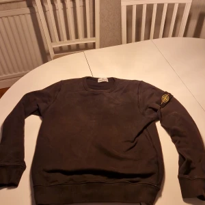 Svart sweatshirt från Stone Island - Snygg mörkgrå sweatshirt från Stone Island Junior med klassisk rund halsringning och ikonisk logotyp-patch på vänster ärm. Tröjan har en avslappnad passform och är tillverkad i mjukt bomullsmaterial. Perfekt för en stilren och trendig look.