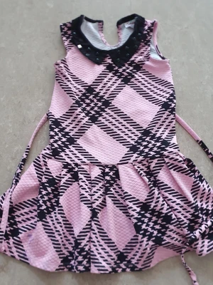 Klänning - Söt kort klänning i rosa och svart med rutigt mönster och dekorativ svart krage med pärlor. Klänningen är ärmlös och har knytband i midjan för extra passform. Perfekt för dig som gillar en lekfull och trendig stil. Den har fläckar av bläck.