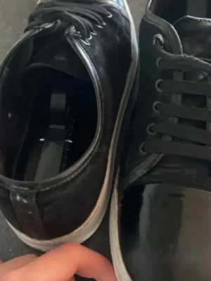 Svarta sneakers från Lanvin - Snygga svarta sneakers från Lanvin med klassisk låg profil. Skorna har svarta snören, rund tå. Skorna är andvända men har inte många tydliga defekter. Inget som inte syns på bilderna. Dem har mycket kvar att ge. Sulan är målad med skofärg som lätt går att aplicera.  Hör av dig vid frågor :)