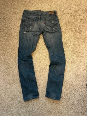 Levis jeans - Snygga blå jeans från Levis med klassiska fem fickor. Jeansen har slitna detaljer och kontrastsömmar, samt logga på bakfickan. Perfekta för en avslappnad och trendig stil.