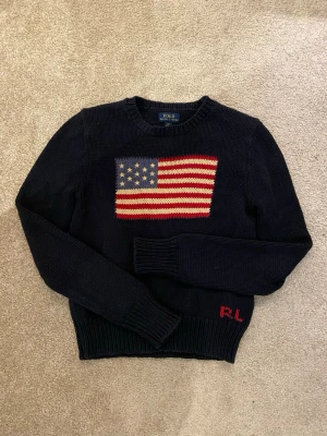 Polo Ralph Lauren stickad tröja 🇺🇸 - Marinblå stickad tröja från Polo Ralph Lauren med klassisk amerikansk flagga broderad på bröstet och liten RL-logga nere vid kanten. Tidlös och populär modell som funkar till det mesta. Väldigt bra skick, inga hål eller fläckar. Storlek 12-14 år men är lite liten i storleken. Skickas samma dag som köpt. Rök- och djurfritt hem🐈🚬. Skriv om frågor uppstår.