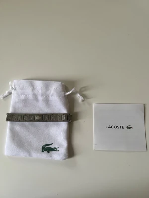 Silverfärgat armband från Lacoste - Snyggt armband i silverfärgad metall från Lacoste med rektangulära länkar och diskret Lacoste-logga. Armbandet har en stilren och modern design, perfekt för att lyfta din outfit med en sportig touch. Levereras med originalpåse och förpackning.
