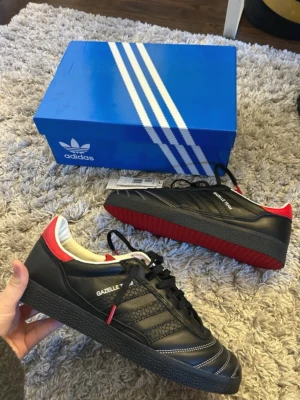 Adidas Gazelle svart/röd sneaker - Snygga Adidas Gazelle sneakers i svart läder med röda detaljer som aldrig används köpta för 700 på rean