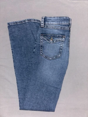 Low waist bootcut jeans - Snygga blå bootcut jeans med klassisk femficksdesign och en extra fickdetalj med knapp bak. Jeansen har en lätt tvättad look och raka ben som blir vidare nedtill. Perfekta för en avslappnad och trendig stil❤️ Är ca 34cm rakt över i midjan och innerbenslängden är ca 81cm. Säljer eftersom de inte längre kommer till användning. Skriv gärna innan ni köper!❤️