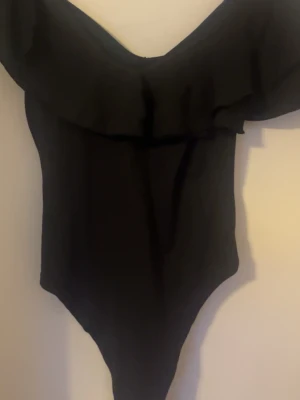 Svart body med volang  - Trendig svart body med off shoulder-design och volangdetalj upptill. Jättefin men måste tyvärr sälja då den var förstor , aldrig använd