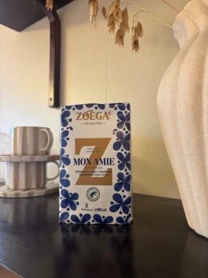 Zoégas Mon Amie jubileumskaffe - Zoégas Mon Amie jubileumsutgåva är ett mörkrostat kaffe med toner av rabarber och viol. Förpackningen är vit med blå blommor och guldiga detaljer, och har en modern, stilren design. Perfekt för dig som gillar unika kaffesorter och snygga förpackningar.