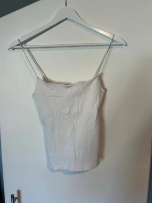 Vit enkel linnetopp med smala band från Zara - Säljer en vit linnetopp med smala axelband och rak passform. Toppen är ärmlös och har en clean, minimalistisk look som passar perfekt till jeans eller kjol. Materialet känns mjukt och lätt, perfekt för varma dagar.