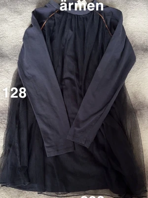 Marinblå  långärmad klänning med tyll - Svart klänning med lång ärm och ett lager av tunn tyll över hela klänningen. Rund halsringning och enkel, rak passform. Perfekt för dig som gillar en stilren look med lite extra volym i kjolen.🌸 Två små hål i ärmen. Storlek 128