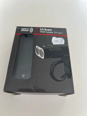 Cykelbelysning set 1000lumen från Urban Safe’n Sound - Cykelbelysning set med framlampa och baklampa. Framlampan har två T6-LED-lampor som ger upp till 1000 lumen.  Den har ett inbyggt batteri på 2400mAh som fungerar som en powerbank och laddas via USB-C.  Baklampan är röd och fästs enkelt på cykeln.  Köpt på cykelverkstad  för 399:- Oöppnad  Djur och rökfritt hem