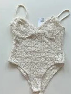 Vit spetsbody med blommönster - Säljer en vit/beige virkad body med blommönster och tunna band.  Perfekt för dig som vill spica upp din stil och göra den lite trendig.