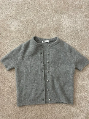 Grå kortärmad kofta från Zara - Supersöt kortärmad grå kofta från Zara! Perfekt att styla över ett linne eller t-shirt eller på egen hand 🥰 säljer då jag inte har plats i garderoben och den inte kommer till användning!
