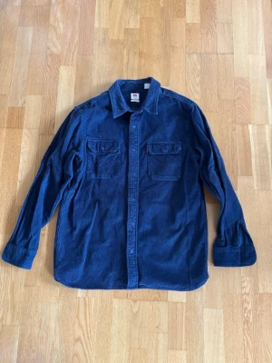 Blå manchesterskjorta från Levi's - Säljer en blå manchesterskjorta från Levi's i relaxed fit. Skjortan har två bröstfickor med knappar och klassisk krage. Perfekt för dig som gillar en avslappnad och stilren look.