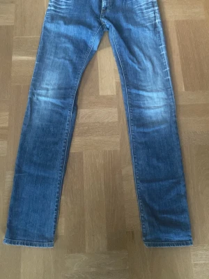 Blå raka replay jeans med slitningar - !Öppen för att sänka priset! Säljer ett par klassiska blå replay jeans med raka ben och snygga slitningar på framsidan. Jeansen har fem fickor och normal midja. Perfekta för en avslappnad och trendig look. Materialet är denim i bomull.