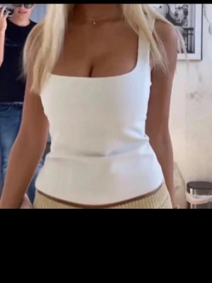 Vit Zara topp - Säljer en snygg vit topp från Zara med fyrkantig halsringning och breda axelband. Toppen är tight och har en stilren design som passar perfekt till jeans eller kjol. Materialet är typ kostym. Endast använd 3 gånger!