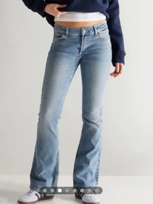 Ljusblå bootcut jeans från junkyard - Säljer ett par ljusblå bootcut jeans från junkyard med klassisk femficksmodell och snygga kontrastsömmar på bakfickorna. Jeansen har normal midja och är tillverkade i mjuk denim med lite stretch för extra komfort.