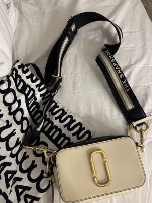 Marc Jacobs Snapshot väska - Snygg beige axelväska från Marc Jacobs med guldiga metalldetaljer. Jätte fin och givetvis äkta. Dustbag kommer med. Bra skick men har lite defekter vid märket längst fram som ni ser på bild 4. Skriv vid frågor❤️