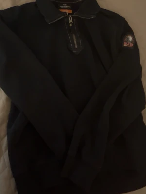 Svart fleece tröja från Parajumpers - Mörk fleece tröja från Parajumpers med dragkedja vid halsen och patch på ärmen. Klassisk krage och diskreta sömmar. Perfekt för lager-på-lager och chill stil. Obs! Den är inte helt äkta men jätte bra kvalité för priset, Storlek L men har tvättats 1 gång så den passar för storlek M och S