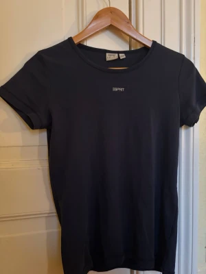 Mörkblå t-shirt från Esprit - Snygg mörkblå t-shirt från Esprit med rund halsringning och vit logotyp på bröstet. T-shirten är enkel och stilren, perfekt för dig som gillar klassiska plagg. Materialet är mjukt och bekvämt bomull. Storlek M, men liten i storlek, närmare storlek S.