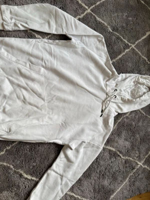 Vit hoodie från Jack & Jones - Snygg vit hoodie från Jack & Jones med klassisk känguruficka och dragsko i huvan. Mjuk insida och avslappnad passform, perfekt för en chill look. Passar till det mesta och är enkel att matcha med andra plagg.