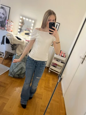 Vit topp med en rosett på ryggen - Säljer en enkel och stilren vit offshoulder topp i mjukt bomullsmaterial. Toppen har korta ärmar och en snygg, tight passform som framhäver axlarna. Perfekt för dig som gillar en clean och modern look. Det är en gullig rosett på ryggen.