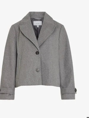 Grå kort kappa från Vila - Stilren grå kappa från Vila med klassisk krage och två knappar framtill. Modellen är kort och har raka ärmar med knappdetalj vid ärmslut. Perfekt för en trendig och clean look. Materialet är mjukt och ger en snygg siluett.