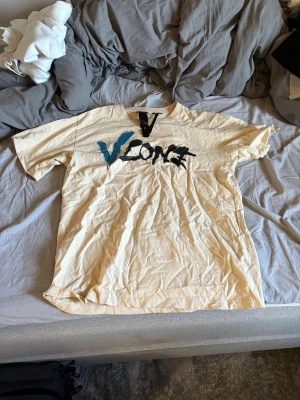 Beige VLONE t-shirt med tryck - Cool beige t-shirt från VLONE med stort svart och blått tryck på bröstet och en stor blå V på ryggen. T-shirten har en avslappnad passform och är tillverkad i mjuk bomull. Perfekt för dig som gillar streetwear och vill sticka ut.