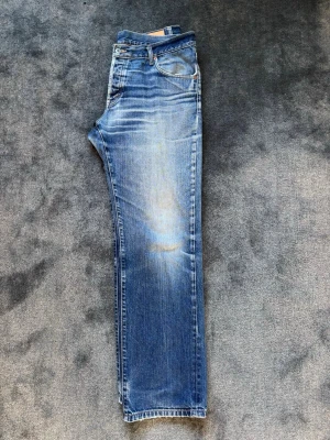 Blå raka jeans med slitningar - Ett par klassiska blå jeans med raka ben och snygga slitningar framtill. Jeansen har fem fickor, normal midja och en lätt tvättad look som ger en avslappnad vibe. Perfekta för dig som gillar en tidlös och enkel stil.