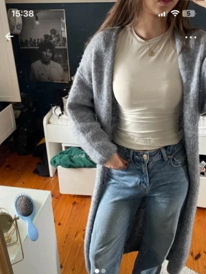 Lång grå stickad kofta  - Lång, öppen grå stickad kofta från Lindex med breda ärmar och mjukt material. Perfekt att slänga över en t-shirt eller topp för en chill look. Koftan har en enkel design utan knappar och är riktigt mysig och varm.