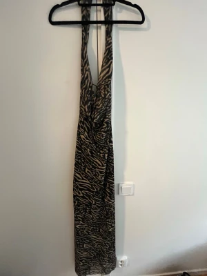 Zebramönstrad långklänning - Säljer en långklänning med zebramönster i svart och beige. Klänningen har djup ringning och en halterneck. Perfekt för bal eller andra tillställningar!