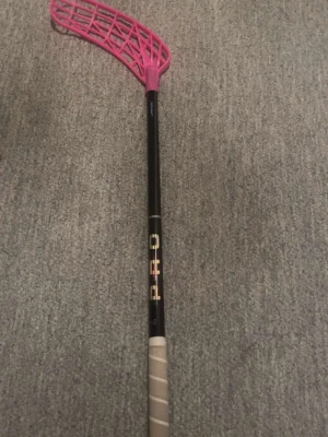 Innebandyklubba med rosa blad - Säljer en innebandyklubba från PRO med svart skaft och ett iögonfallande rosa blad. Skaftet har ett grepp i beige och texten PRO i färgglada bokstäver. Perfekt för dig som gillar innebandy och vill sticka ut på planen.