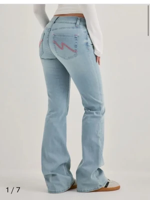 Ljusblå bootcut jeans med brodyr - Snygga ljusblå bootcut jeans med rosa broderade blixtar på bakfickorna. Jeansen har klassisk femficksdesign och normal midja. Perfekta för dig som gillar en retroinspirerad look och vill sticka ut lite extra.