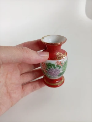 Liten japansk porslinsvas med blommor - Söt liten vas i porslin med handmålat blommönster i grönt, lila och rött. Vasen har gulddetaljer och en klassisk form med bred öppning. Märkt 'Äkta Japanskt' undertill. Perfekt som dekoration eller samlarobjekt.