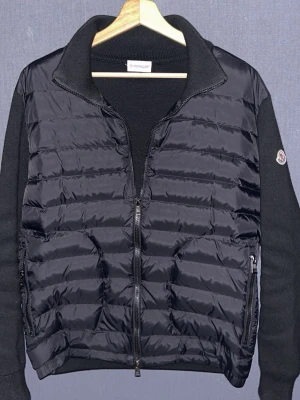 Svart Moncler Cardigan  - Snygg svart cardigan från Moncler med quiltad front och stickade ärmar. Jackan har dragkedja framtill, hög krage och två fickor med dragkedja. Scan funkar. Passar S/M