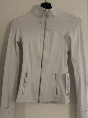 Lululemon light Ivory - Jätte fin lululemon define jacket i färgen light Ivory med guld detaljer. Den är full lenght och i storlek 2. Inga defekter!! Lappen är dessvärre av då jag tog dessa bilder när precis kom, den är dock i samma skick💗💗 skulle säga att färgen är mellan beige/vit (Jätte svår att få tag på😇)