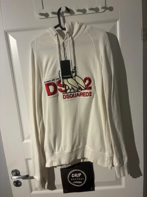 Vit hoodie från Dsquared2 med tryck - Snygg vit hoodie från Dsquared2 med broderat DSQ2-tryck och duva på bröstet. Klassisk modell med huva och dragsnören, samt ribbade muddar vid ärmslut och midja. Perfekt för dig som gillar streetwear och vill sticka ut med en exklusiv look.