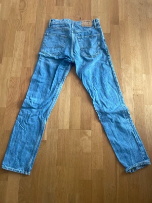 Blå raka jeans från Levi's - Säljer ett par klassiska blå jeans från Levi's med raka ben och femficksdesign. Jeansen har en ljusblå tvätt och är tillverkade i slitstark denim. Perfekta för dig som gillar en tidlös och avslappnad look.