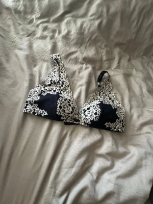 Svart spetsbralette med vit brodyr - En snygg svart bralette med triangelformade kupor och dekorativ vit spetsbrodyr. Bh:n har tunna axelband och är utan bygel för en bekväm känsla. Materialet är mjukt och stretchigt, perfekt för dig som gillar en feminin och trendig stil.