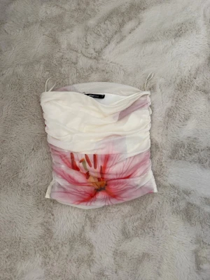 Vit bandeau topp med blommönster - Trendig vit bandeau topp med ett stort rosa blommönster framtill. Den är ärmlös och har en croppad passform.