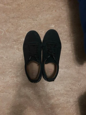 Svarta Louboutin sneakers med röd sula - Svarta sneakers från Christian Louboutin med klassisk röd sula och svarta skosnören. Ovandelen är i mocka och insidan har en beige innersula. Snygg och stilren design med låg profil och diskreta detaljer.