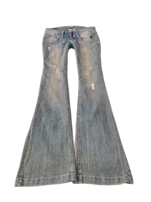 Ljusblå utsvängda jeans  - Snygga ljusblå jeans  med låg midja och extra utsvängda ben. Jeansen har slitna detaljer och tre knappar framtill. Perfekta för dig som gillar retrostil och vill sticka ut med en cool siluett.