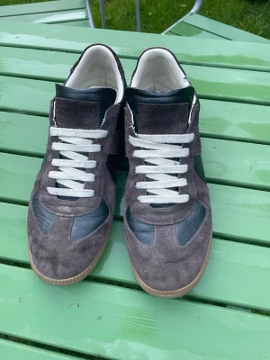Maison margiela gats - Snygga Maison margiela sneakers i brun mocka och svart läder med vita skosnören och klassisk gummisula. Modellen har lågt skaft och en stilren design som passar till det mesta. Perfekta för dig som gillar en clean och tidlös look.