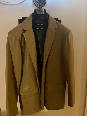 Beige skinnjacka från Gatto - Stilren beige skinnjacka från Gatto med klassisk kavajkrage och två framfickor. Jackan har en rak passform och slät yta, perfekt för dig som gillar en clean och modern look.