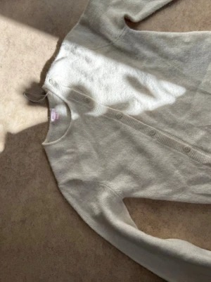 Ljusbeige kofta med rund hals - Mysig ljusbeige kofta med rund halsringning och knappar framtill. Tillverkad i ett mjukt, fluffigt material som ger en avslappnad look. Långärmad modell som passar perfekt till lager på lager-stil.