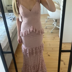 Ljusrosa långklänning med volang och spets - Romantisk ljusrosa långklänning med volangdetaljer och spets. Djup v-ringning, ärmlös design och öppen rygg med snörning. Perfekt för speciella tillfällen när du vill sticka ut. Slutsåld i flesta storlekarna💗