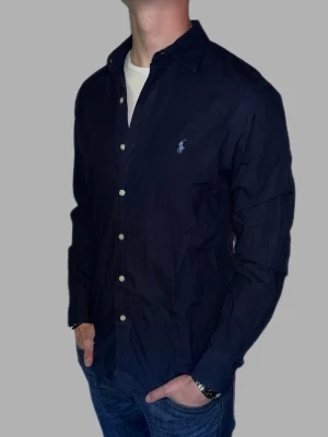 Mörkblå skjorta från Ralph Lauren - 🔹 Märke: Ralph Lauren 🔹 Modell: Skjorta 🔹 Storlek: M 🔹 Färg: Mörkblå 🔹 Skick: Väldigt fint skick 🔹 Passform: Slim fit 🔹 Pris: 349kr  ✅ 100% äkta ✅ Snabb frakt ✅ Fler bilder/video finns vid intresse ✅ Stilren och lättmatchad