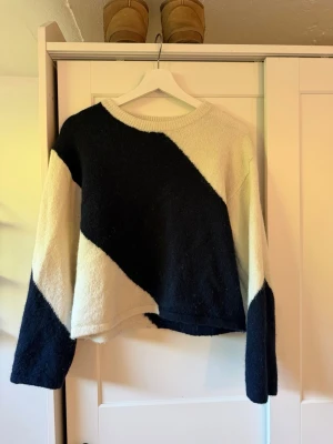 Svartvit stickad tröja med mönster - Cool stickad tröja i svart och vitt med stora diagonala blockmönster. Tröjan har rund halsringning, långa ärmar och en avslappnad passform. Perfekt för dig som gillar en stilren men ändå unik look. Materialet känns mjukt och skönt mot huden.