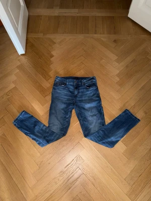 Blå jeans från Tommy Hilfiger - Snygga blå jeans från Tommy Hilfiger med klassisk femficksdesign och raka ben. Jeansen har röda sömmar på insidan av linningen och är tillverkade i ett slitstarkt denimtyg. Perfekta för en avslappnad och trendig look.