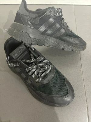 Svarta Adidas sneakers med mesh och läder - Säljer ett par svarta Adidas sneakers med cool design. Skorna har ovandel i mesh och läderdetaljer, samt de klassiska tre ränderna på sidan. Tjock sula och svartvita snören ger en sportig vibe. Perfekta för dig som gillar streetwear och vill ha något bekvämt och snyggt. Inte använd dom alls så mycket inga skador eller något fraktar samma dag 