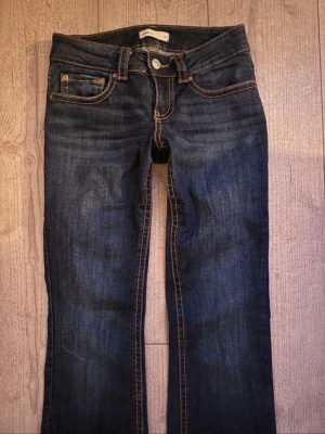 Mörkblå låg midja bootcut jeans - Snygga mörkblåa låg midja bootcut jeans från Gina Tricot. Jeansen har klassiska knappbackfickor på baksidan. Storleken är 34/XS och löngsen är ungefär 160cm-165cm. En trendig utseende!
