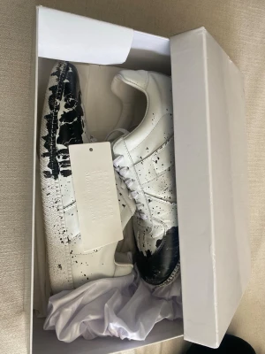 Masion margiela svart vita  - Säljer ett par Masion margiela med svart detaljering, säljer dom lite billigare pga av skadorna av den svarta färger annars har jag bara andvända skorna 3 gånger om man ska vara exakt. Jag kan tvätta skorna innan vid köp! Skriv vid frågor eller funderingar, ska försöka svara så snabbt som möjligt! 